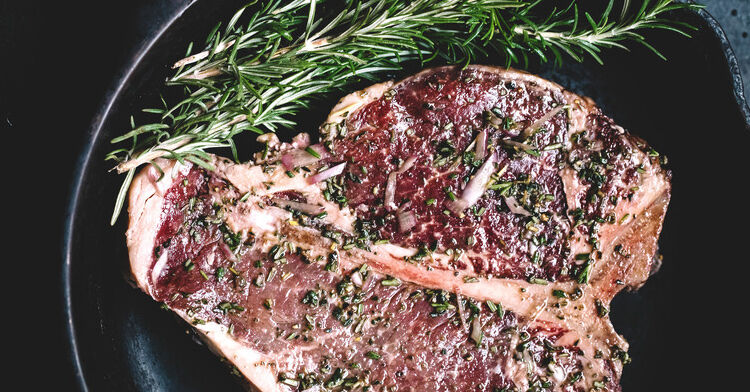 A raw porterhouse steak on a plate with a stem of rosemary